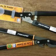 Two black Fiskars pruning shears on a tan surface, with orange and white packaging nearby