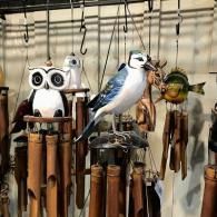 Decorative owl wind chimes hanging outdoors, including a blue bird and a green bird figurine