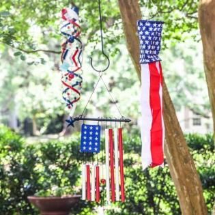 Patriotic red, white, and blue hanging wind chimes and an American flag in a leafy yard