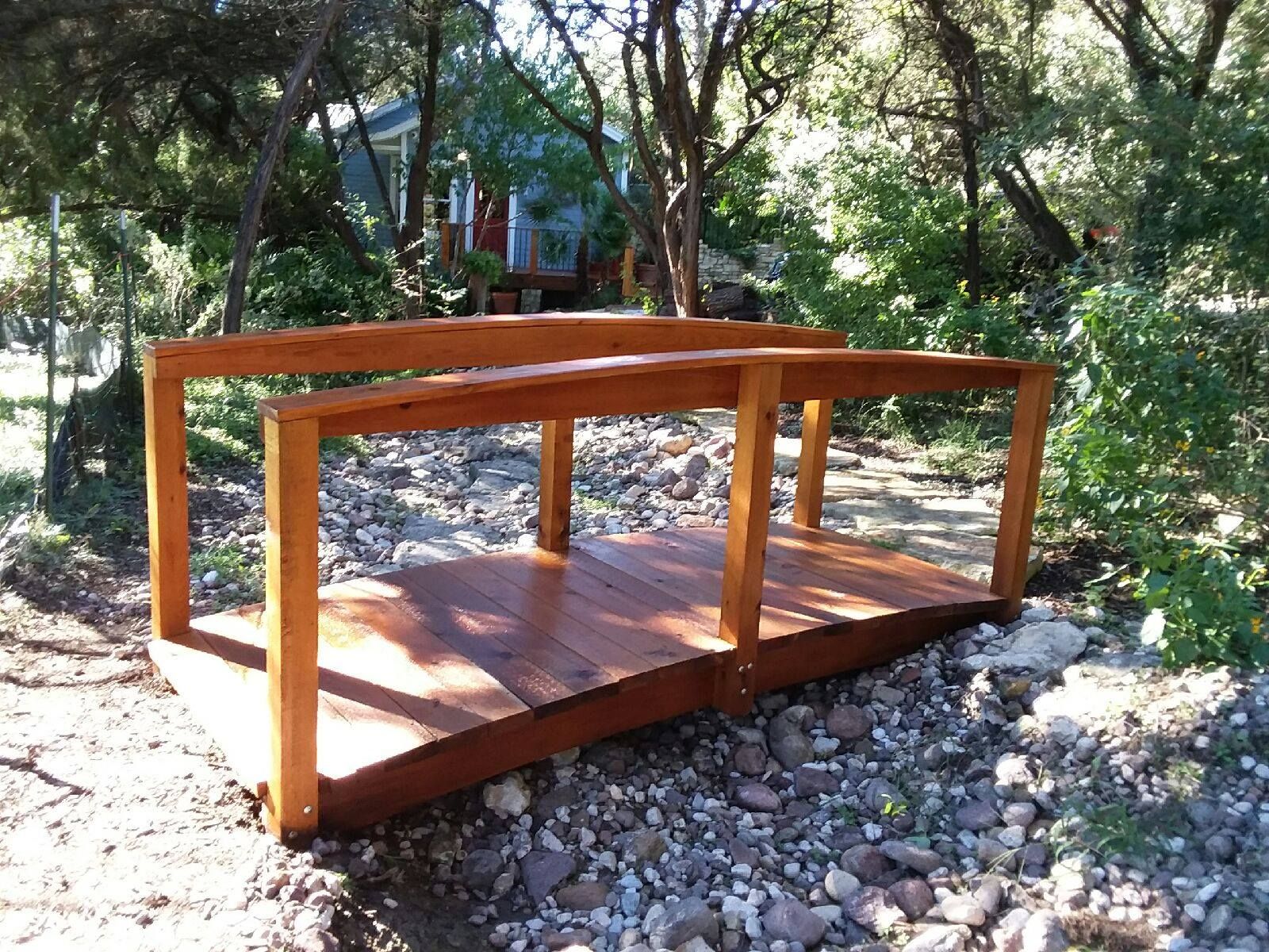 Wooden footbridge over a rocky creek bed, surrounded by trees and greenery.