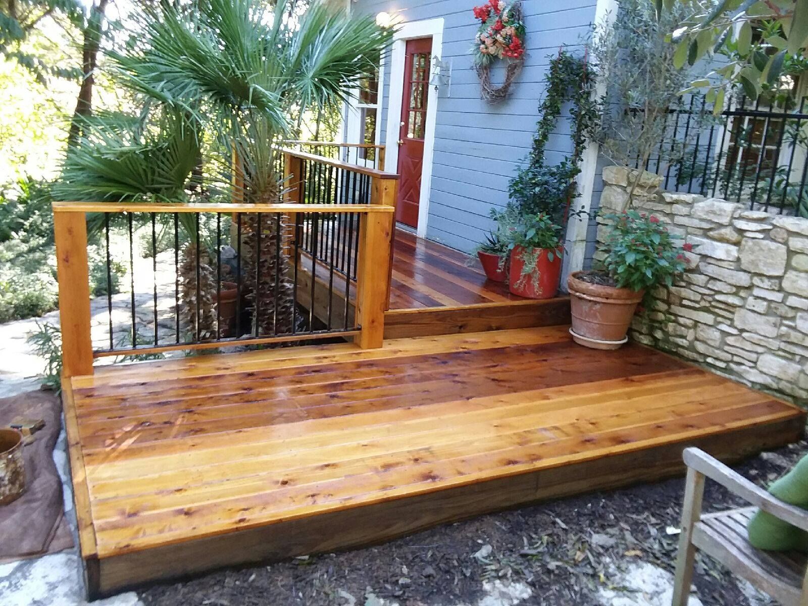 Wooden deck with brown railings, leading to a small blue house with a red door. Palm tree nearby.