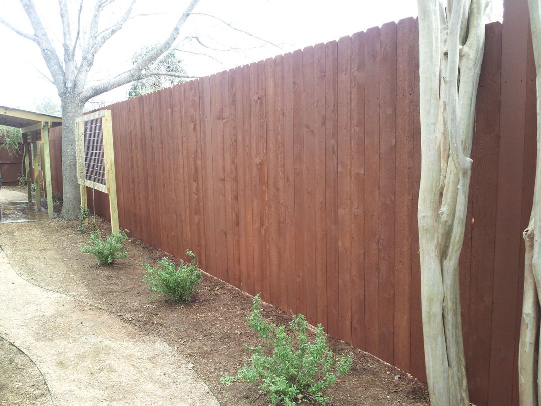 Brown wooden fence bordering a garden bed with small green plants and a pathway.