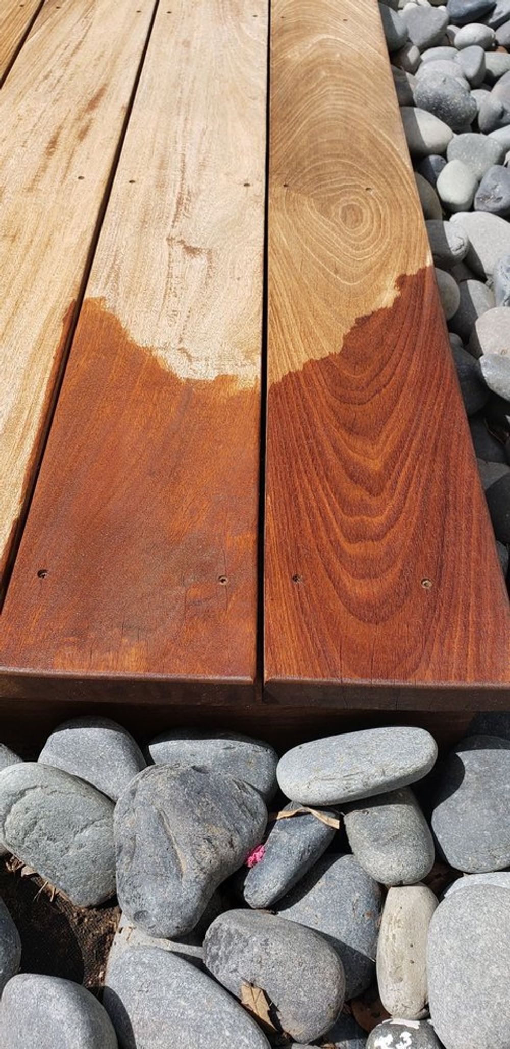Wooden planks, half stained with a reddish-brown color, rest on pebbles.