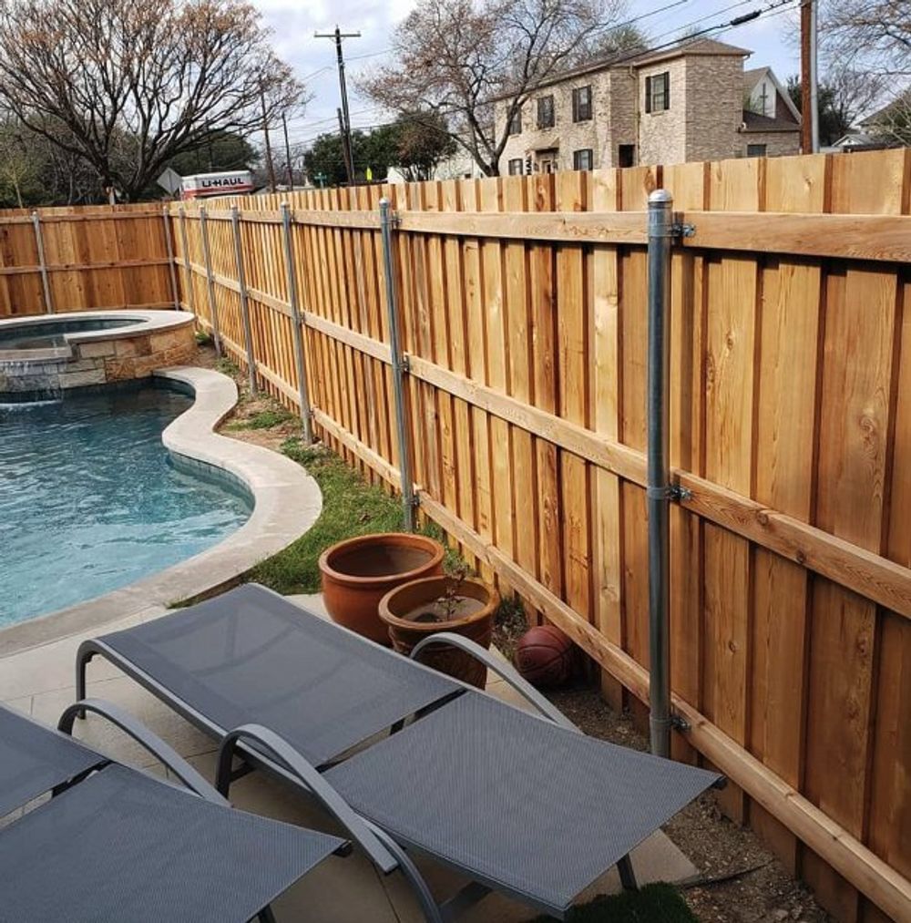 Wooden fence beside a pool with lounge chairs.