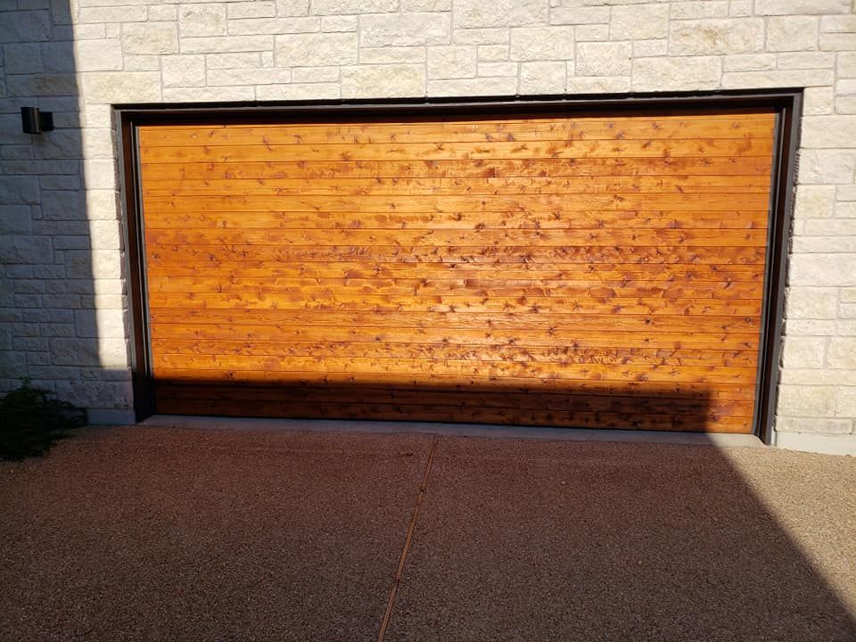 Wooden garage door with dark frame, set in brick wall, on a stone driveway.