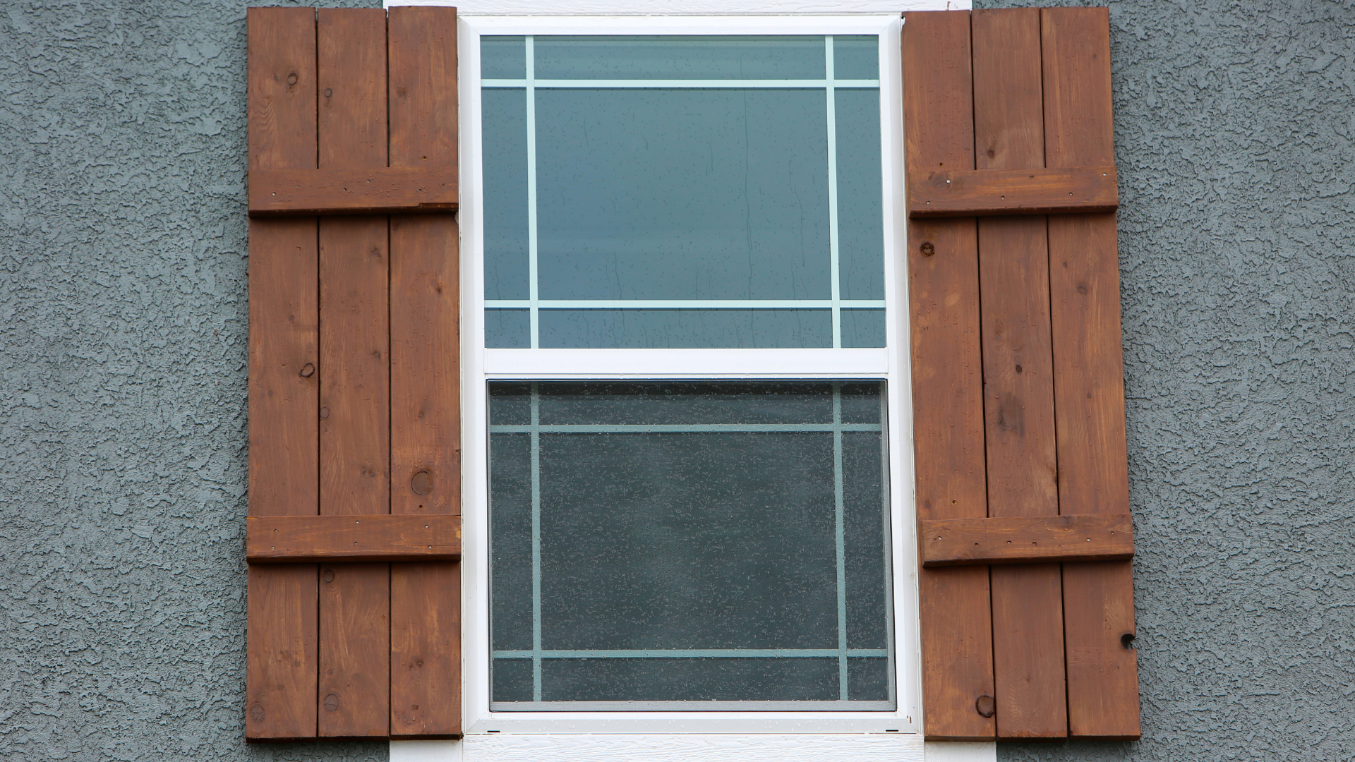 Window with brown wooden shutters on a gray stucco wall.