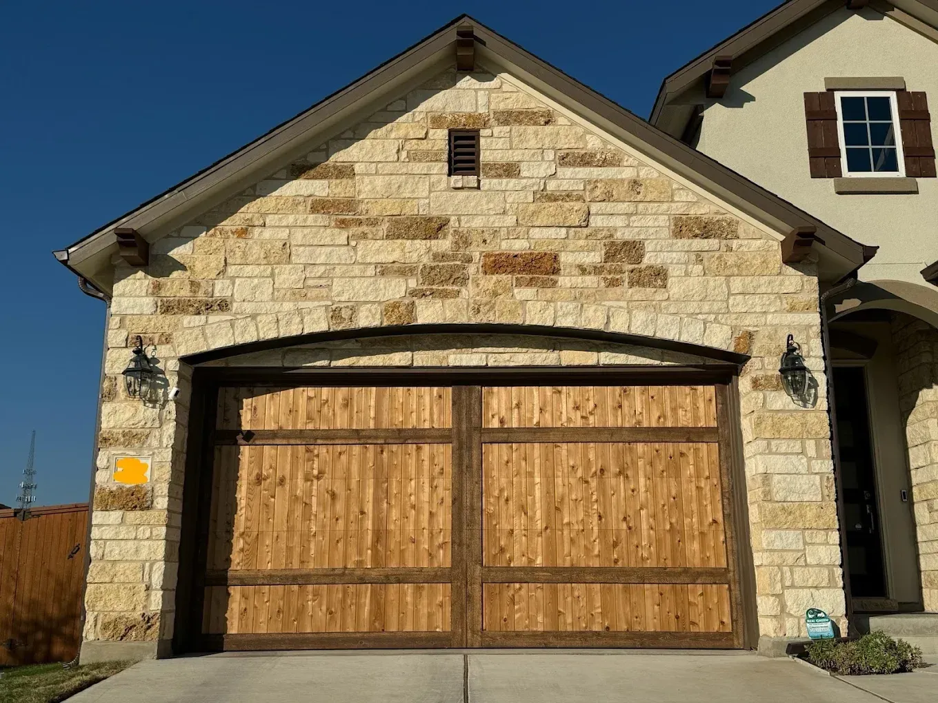 Garage with stone facade, arched doorway, and wooden garage doors under a blue sky.