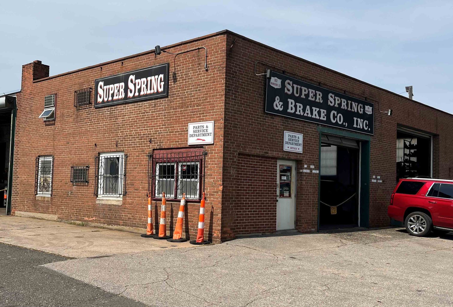 A Red Car Is Parked In Front Of A Brick Building — Hartford, CT — Super Spring & Brake Co., Inc.
