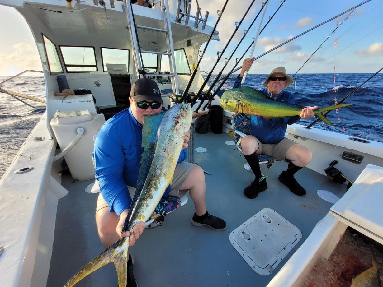 Two people holding large mahi-mahi fish on the deck of a boat on the ocean.