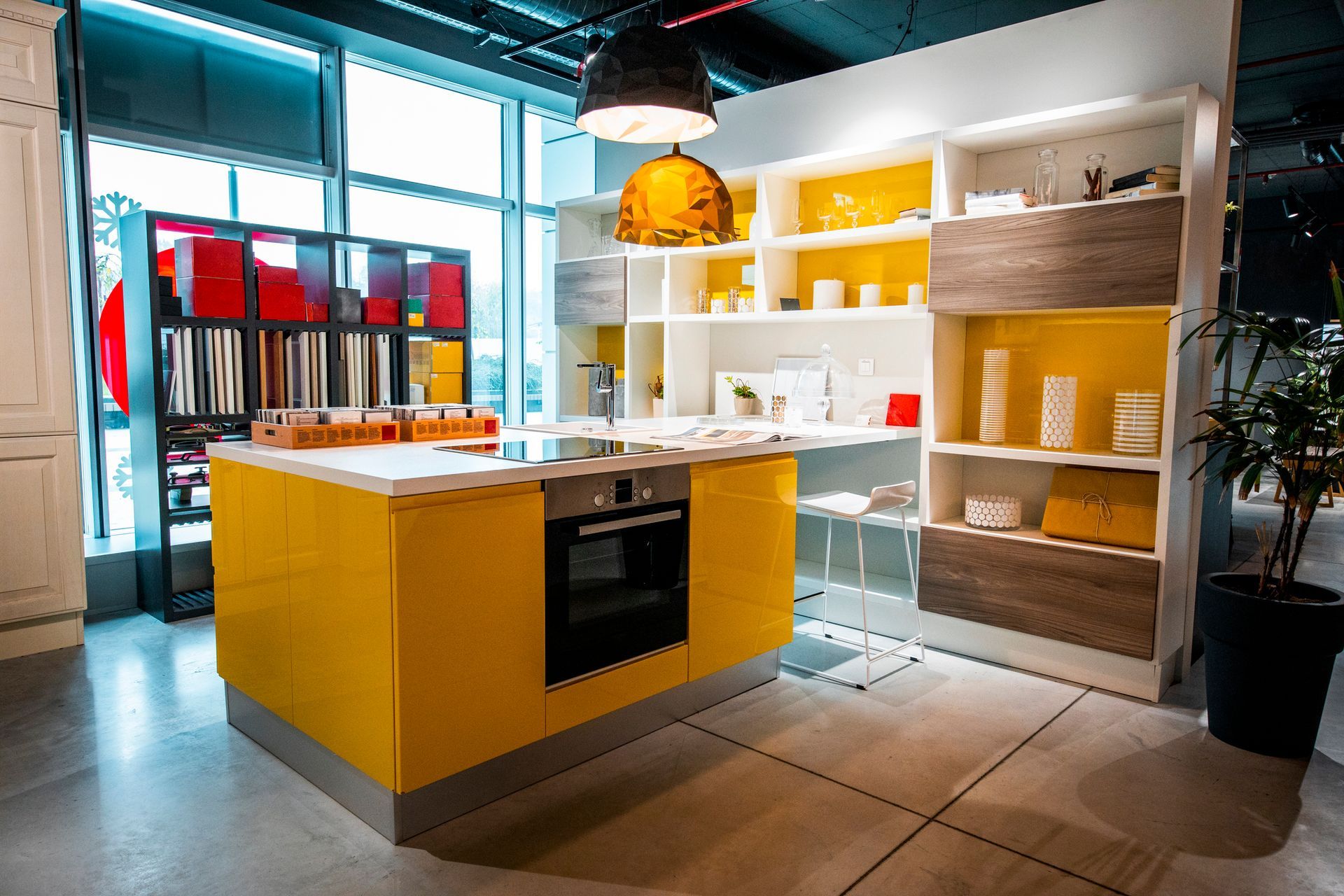 A modern kitchen display with a yellow island, white shelves, and large windows. Yellow accents contrast against white and brown.