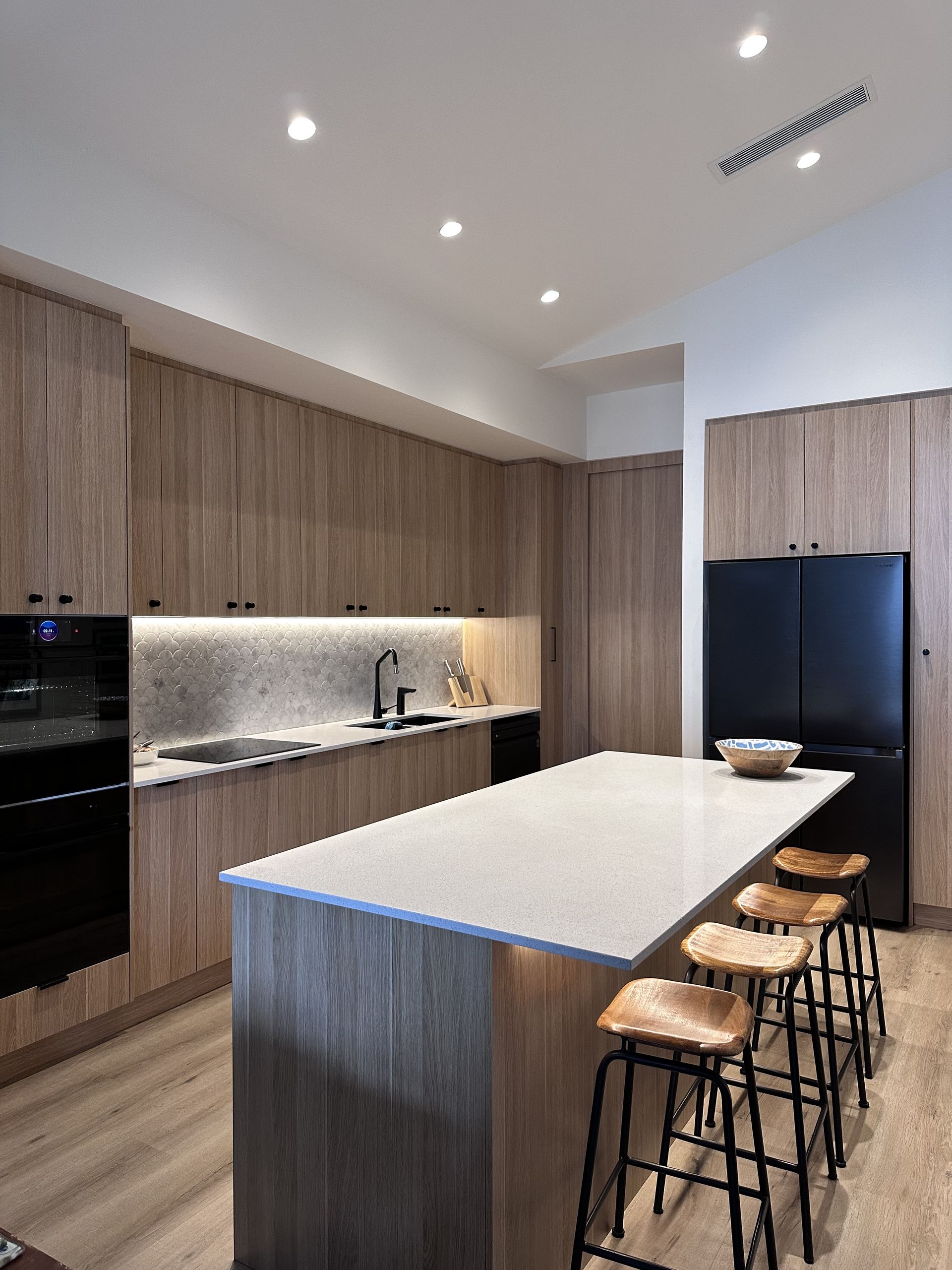Modern kitchen with wooden cabinets, island with stools, and black appliances.