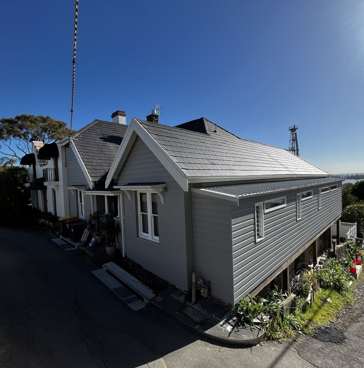 Gray house with a dark roof on a hill under a clear blue sky.