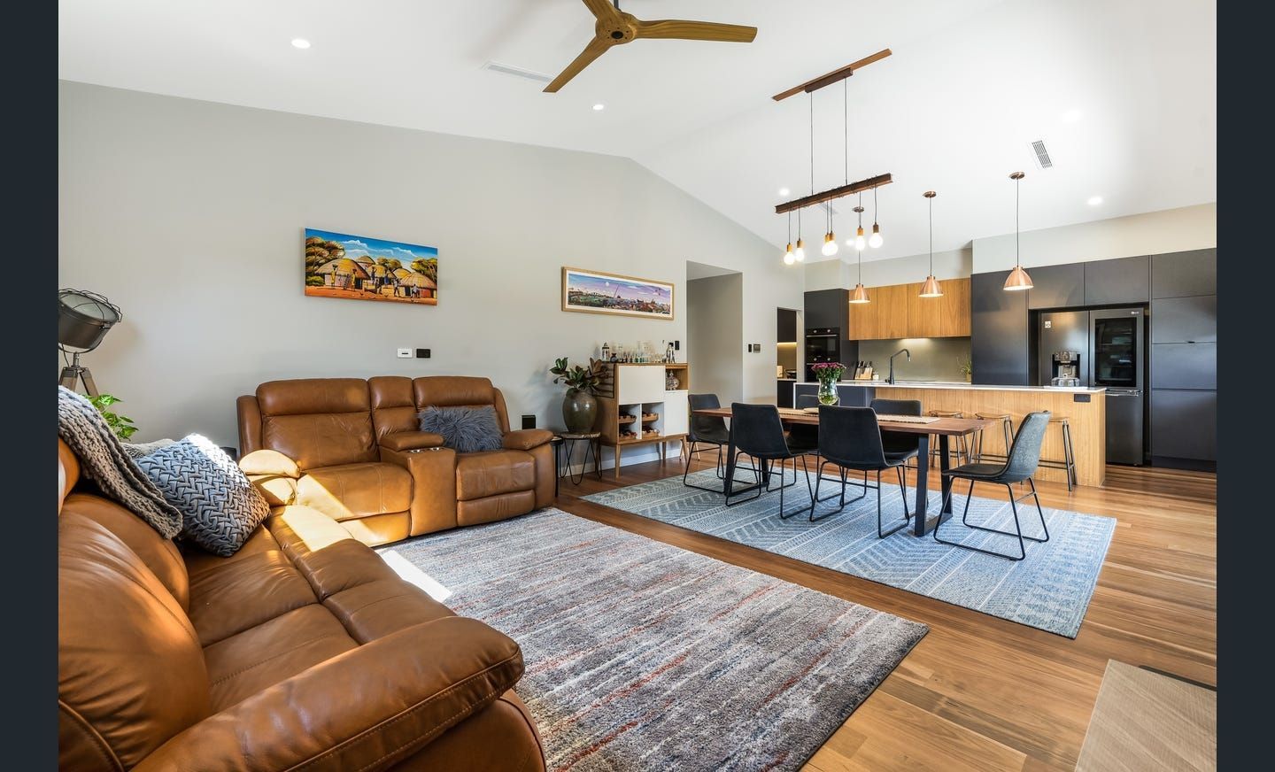 Living room with brown leather sofa, dining table, and kitchen with gray cabinets.