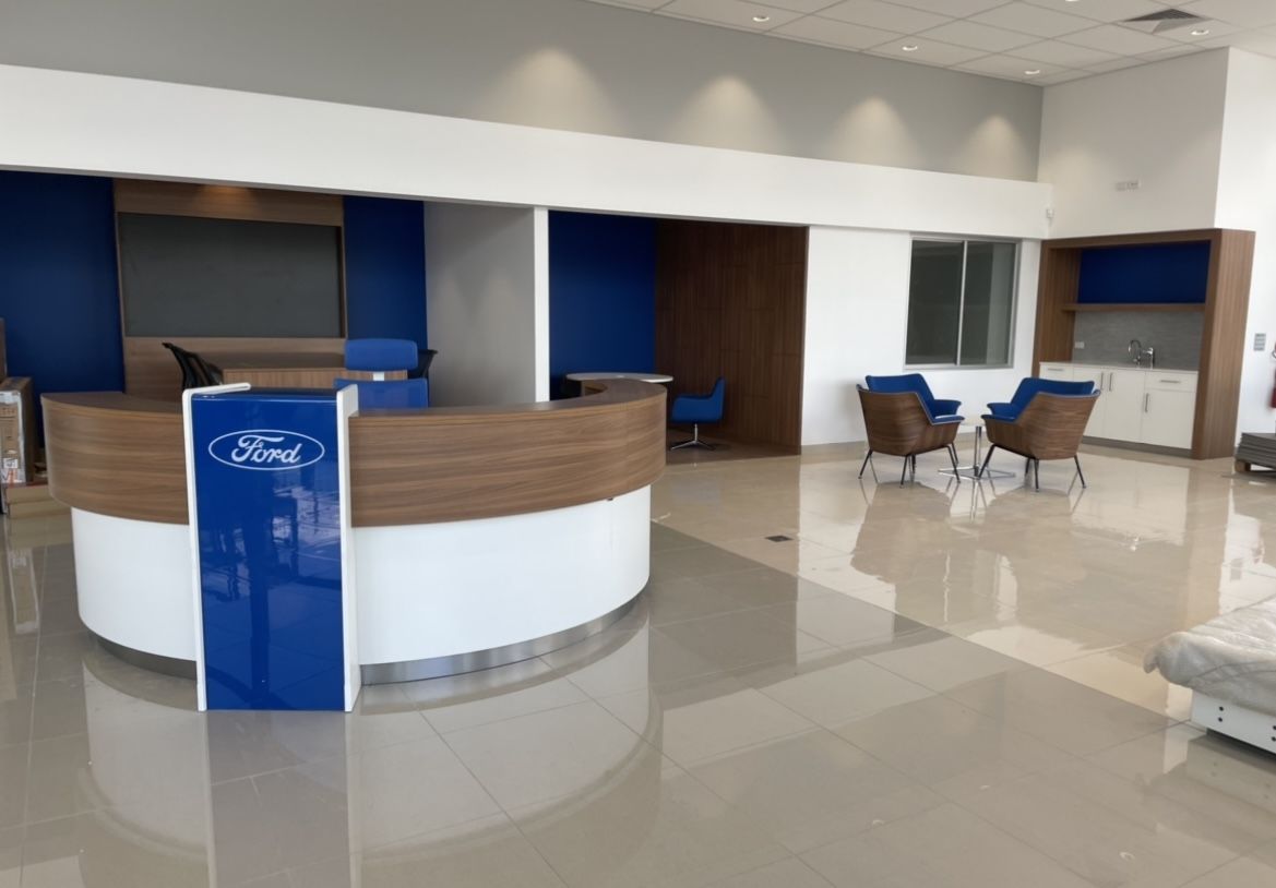 Ford dealership interior with reception desk and waiting area, featuring blue and wood accents.
