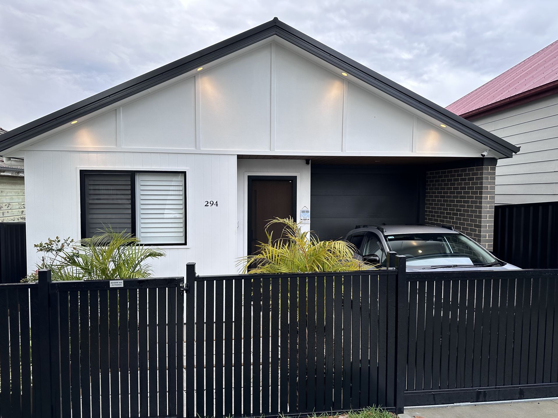 White house with black trim, a black fence, and a car in the garage.