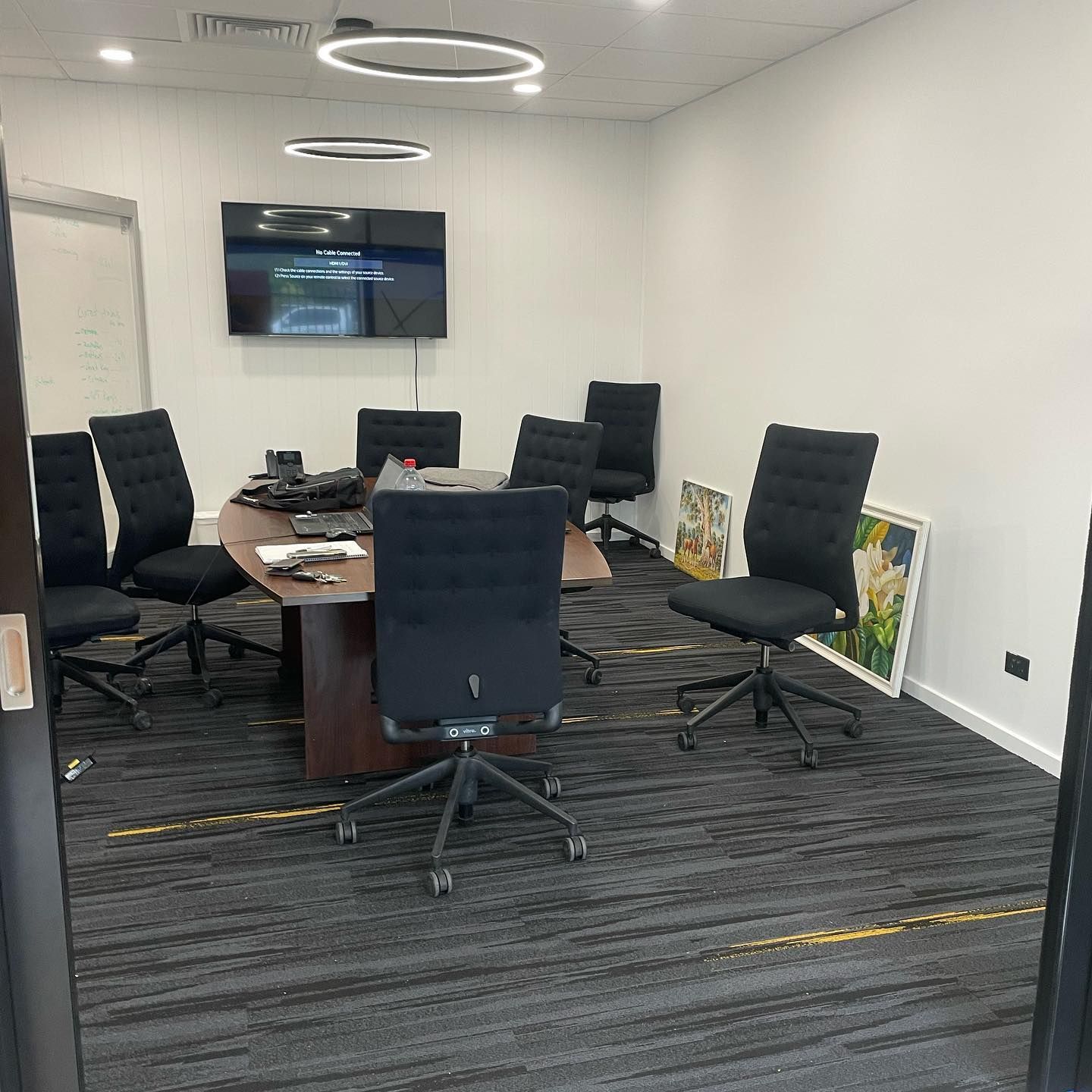 A Conference Room With a Large Oval Table, Eight Black Chairs, a Tv, and Carpeted Floor — Rowal Constructions in Kotara, NSW