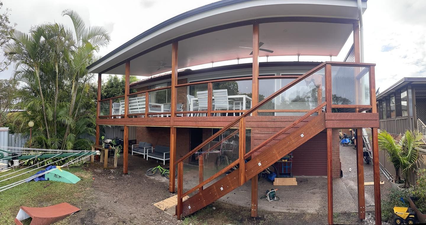 Two-story Wooden Deck With Glass Railing, Stairs, and a Curved Roof — Rowal Constructions in Cardiff, NSW