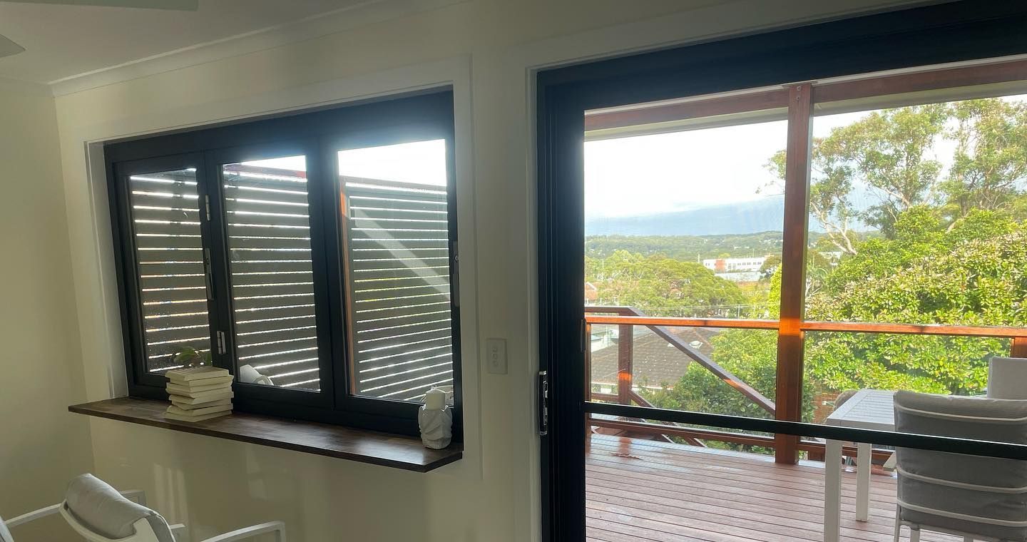 A window and sliding door with black frames. The view includes a balcony, trees, and a distant landscape.