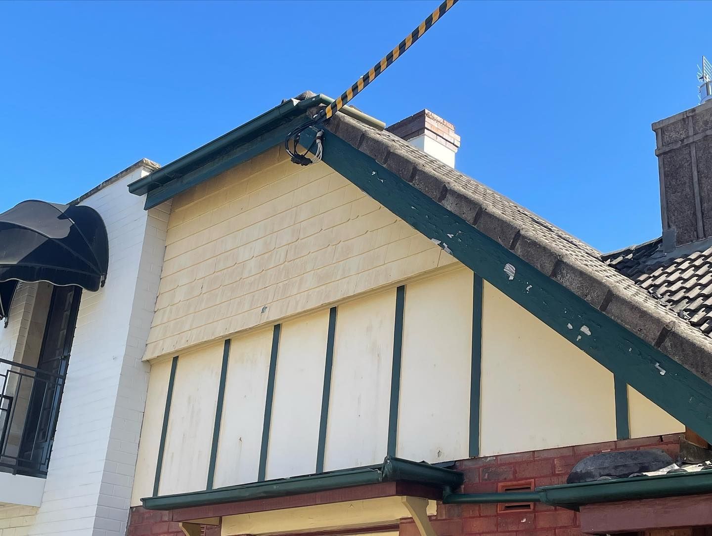 Angled house facade with brick, cream siding, green trim, and brown roof under a blue sky.