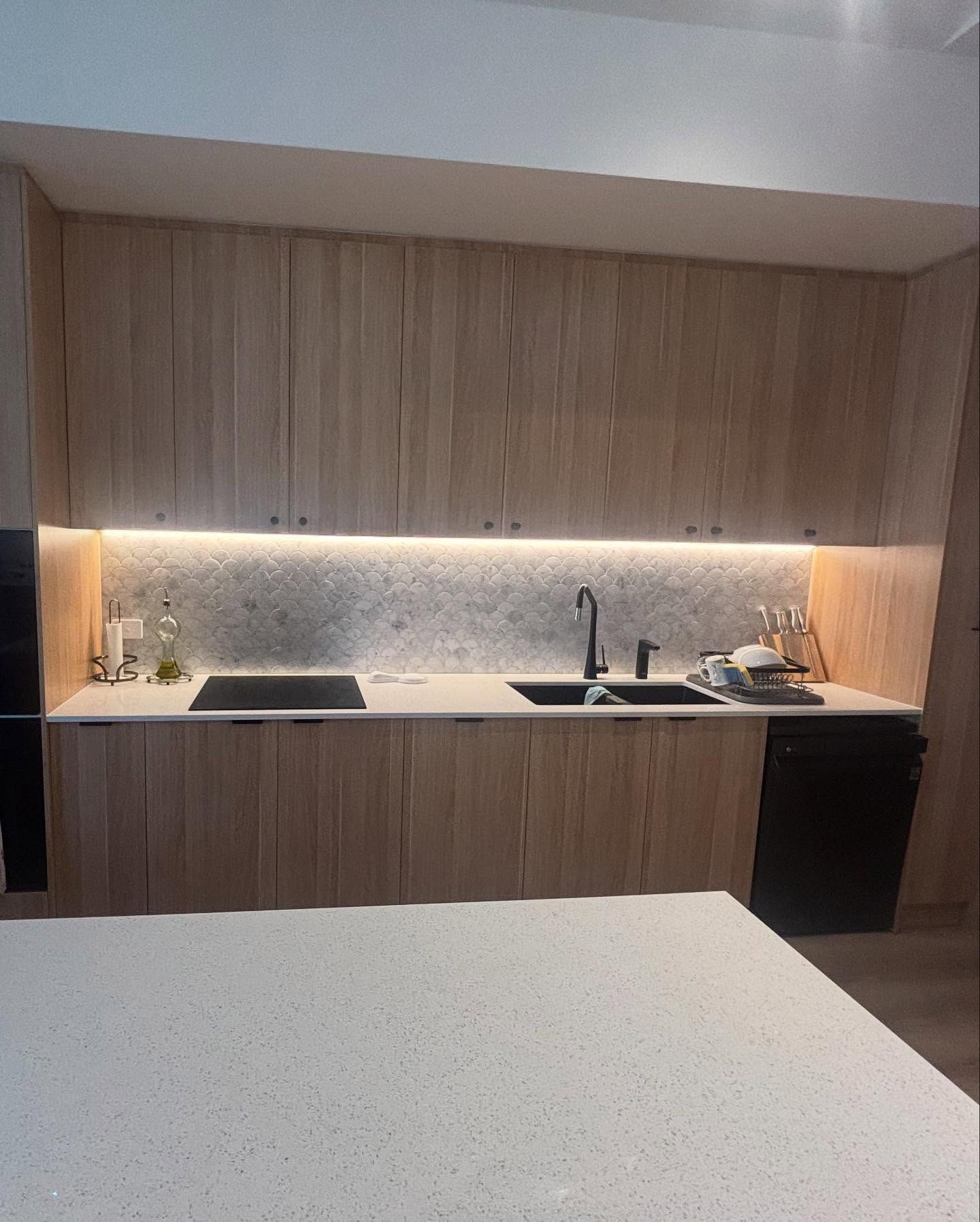 Modern Kitchen With Light Wood Cabinets, Black Appliances, and Countertop — Rowal Constructions in Wallsend, NSW