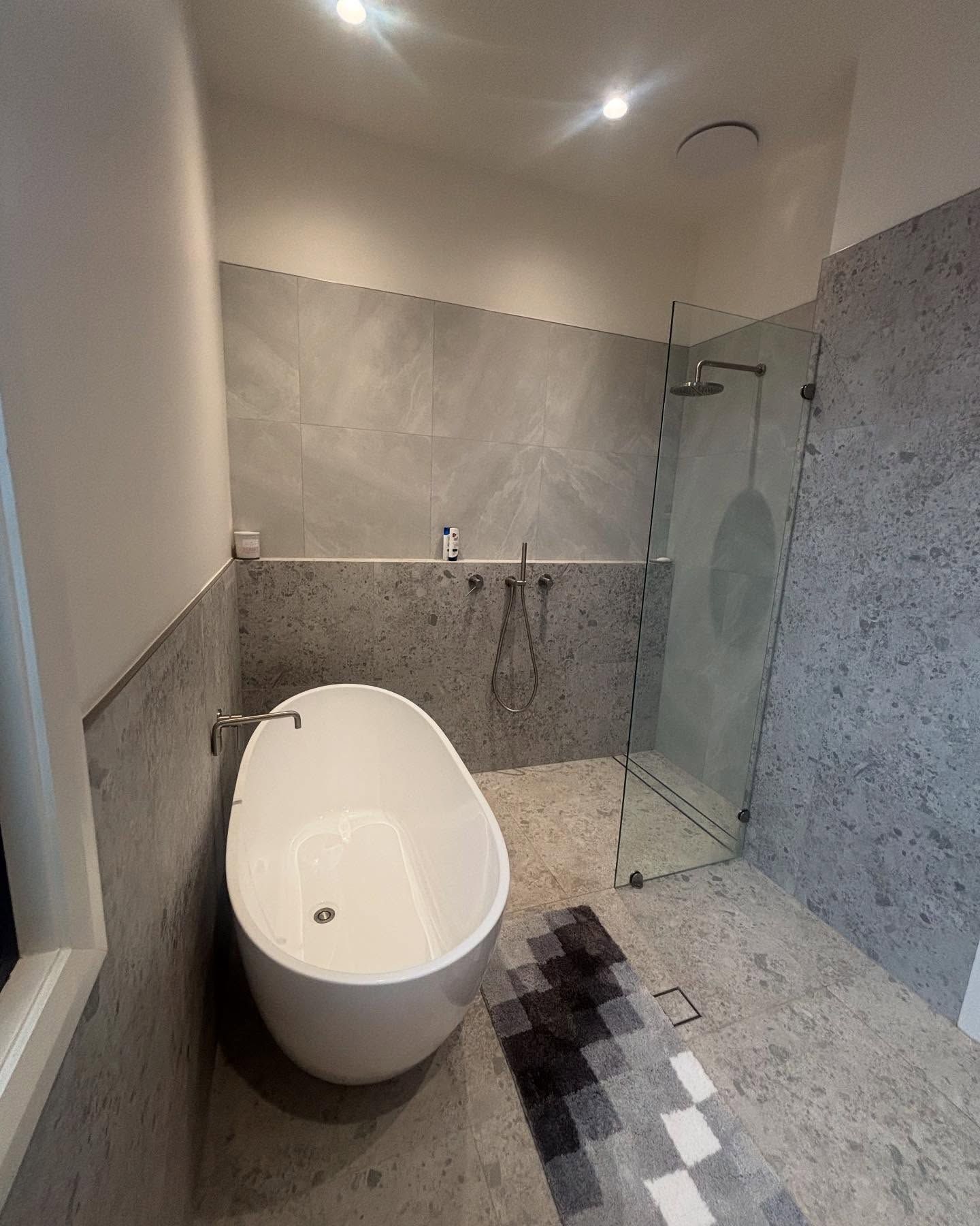 Modern Bathroom With a White Oval Bathtub, Glass Shower, and Gray Walls and Floor — Rowal Constructions in New Lambton, NSW