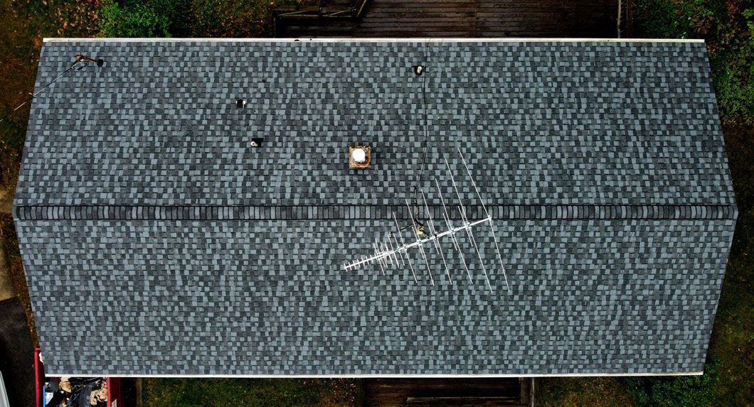 Aerial view of a gray shingled rectangular roof with a chimney and an antenna.