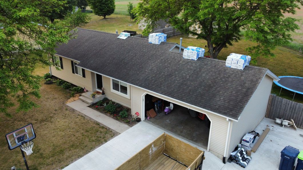 An aerial view of a tan single-story house with shingles staged on the roof for a residential roof replacement.