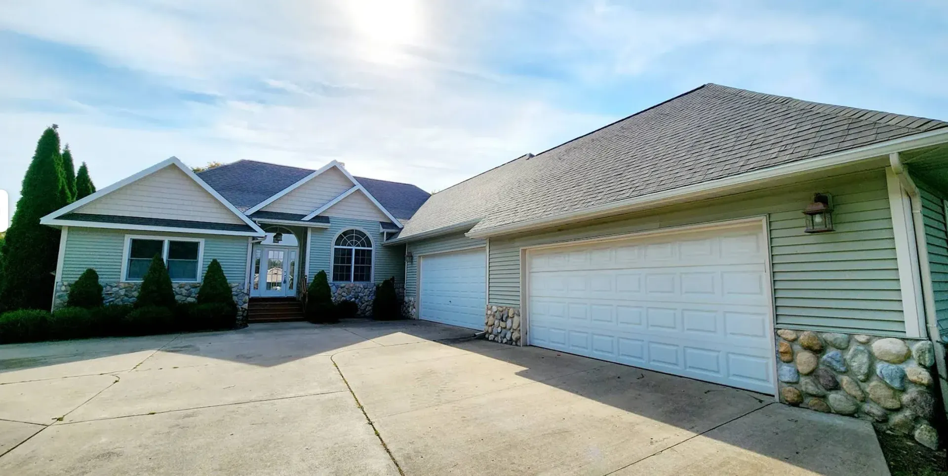 A single-story house with light-colored siding, stone accents, a large three-car garage, and a concrete driveway.
