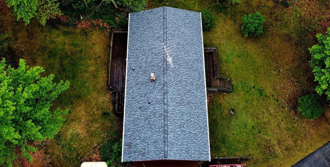 An aerial view of a rectangular, gray-roofed structure surrounded by a lush green lawn and trees.