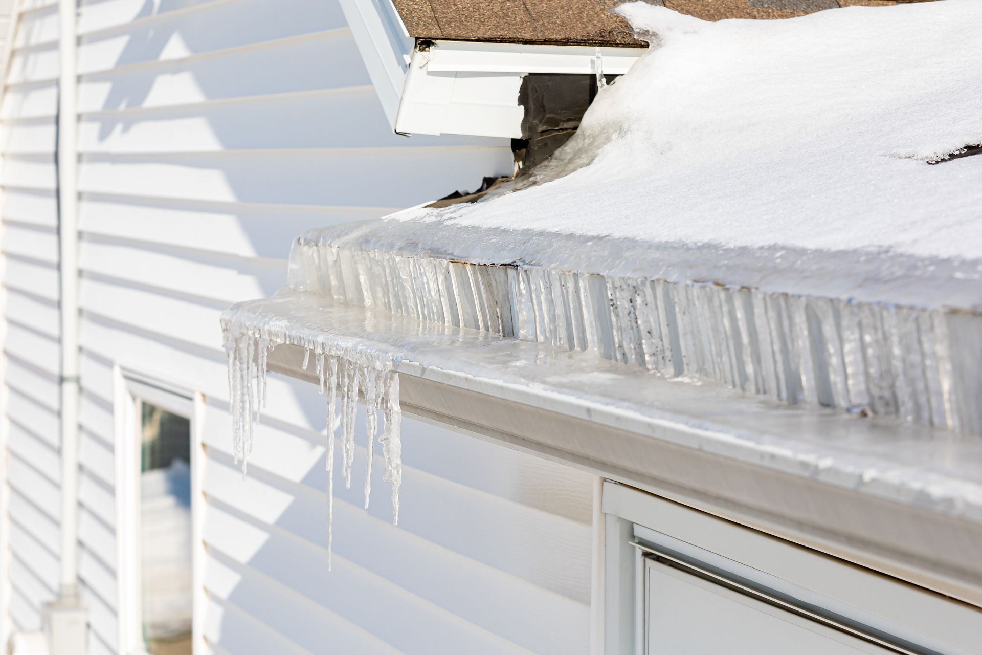 Icicles and a wall of ice formed in the gutters of a house covered in snow.