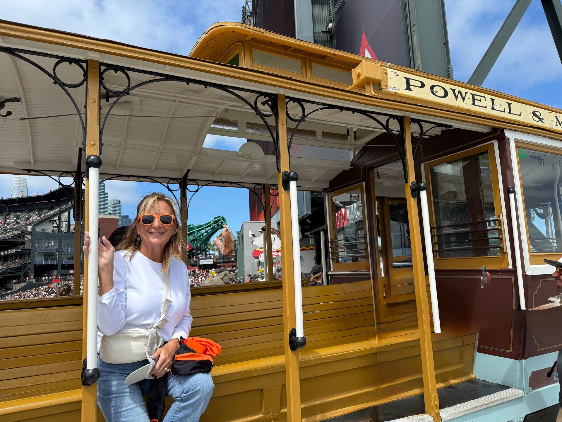 Woman poses next to a San Francisco cable car. Sky, buildings and street visible in the background.