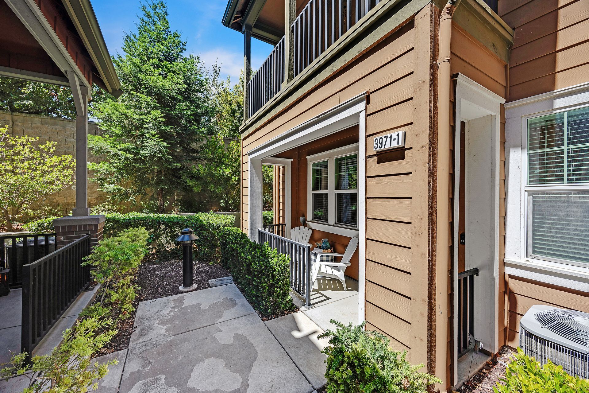Exterior view of a two-story building with a small patio and landscaping, brown siding, and an air conditioning unit.