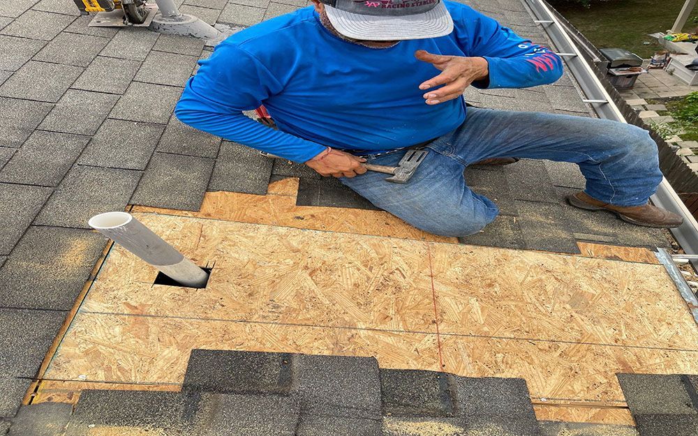 A man in a blue shirt is kneeling on a roof in San Antonio, TX.