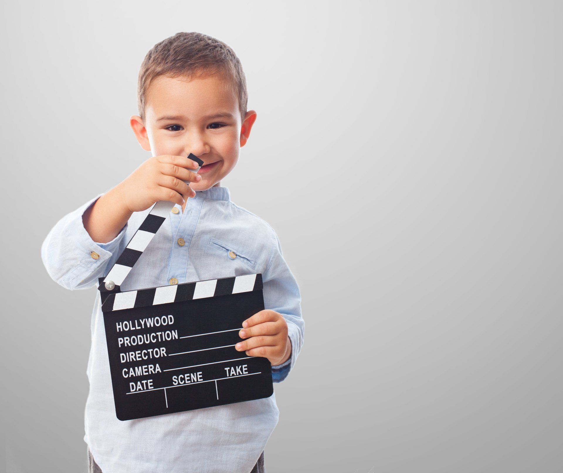 A young boy is holding a clapper board in his hand.