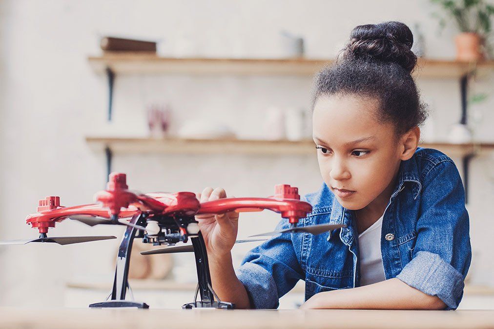 A young girl is sitting at a table playing with a toy drone.