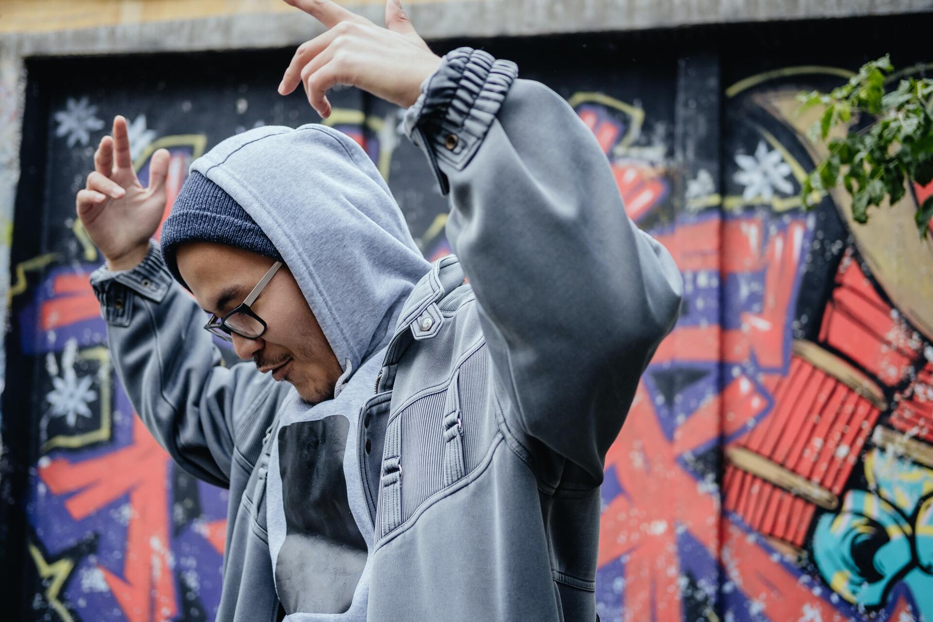A man in a hoodie is dancing in front of a graffiti wall.