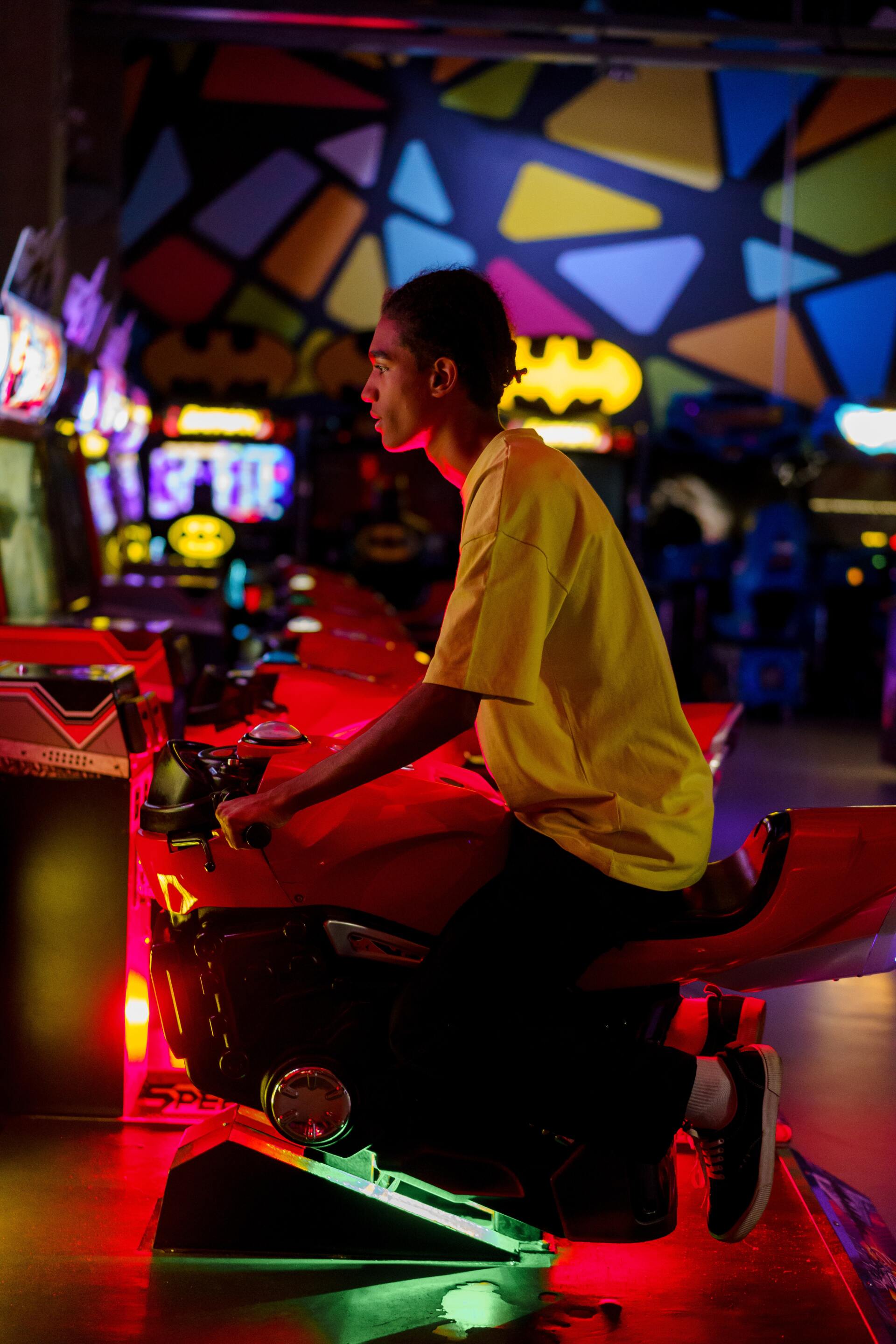 A man is sitting on a red motorcycle in an arcade playing a video game.