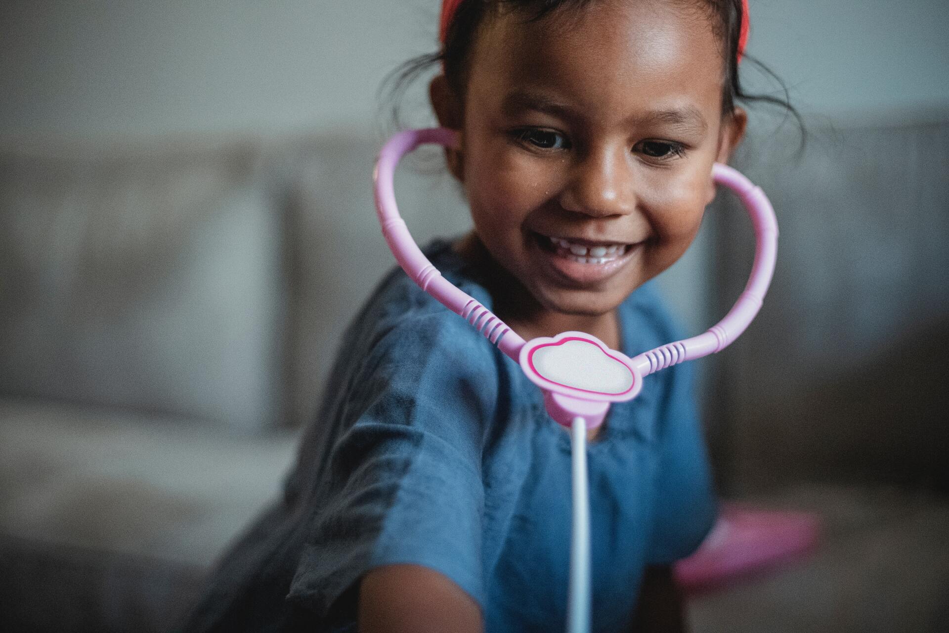 A little girl is wearing a stethoscope around her neck and smiling.