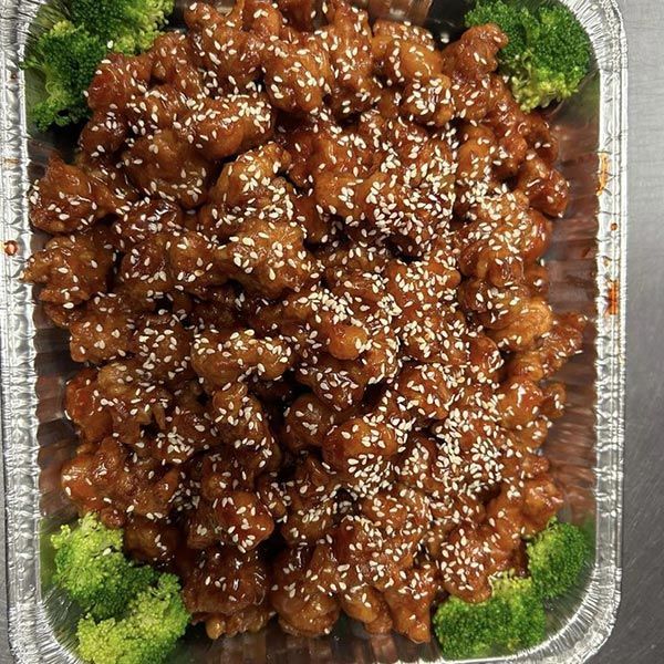 A pan filled with sesame chicken and broccoli on a table.