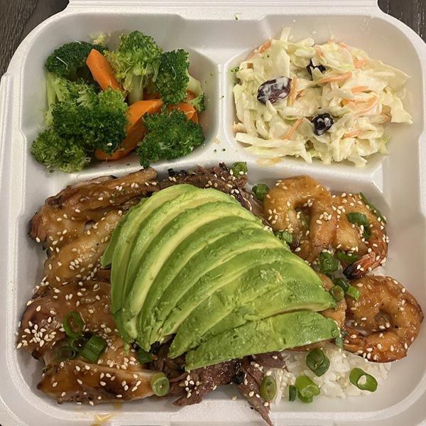 A tray of food with avocado , shrimp , broccoli and coleslaw.
