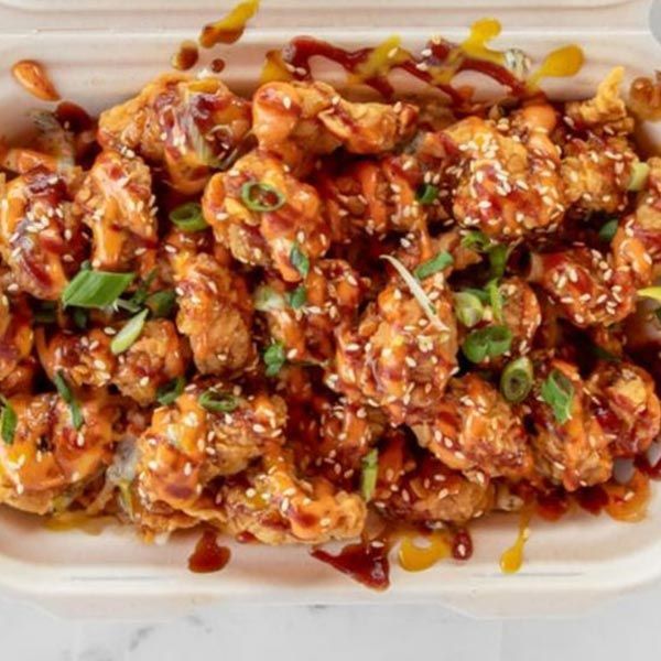 A styrofoam container filled with fried chicken and sauce.