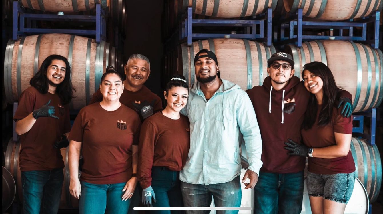A group of people are posing for a picture in front of wine barrels.