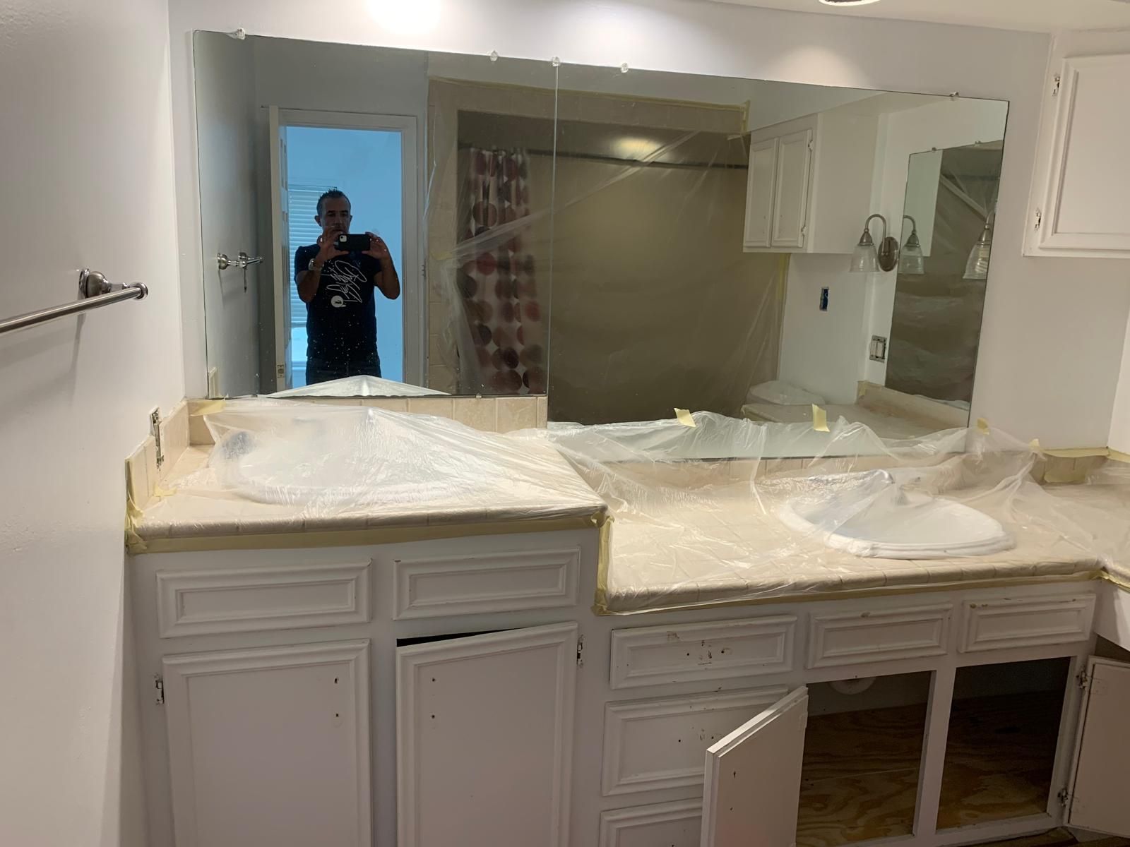 Bathroom with white cabinets, two sinks, large mirror, and open cabinet door.