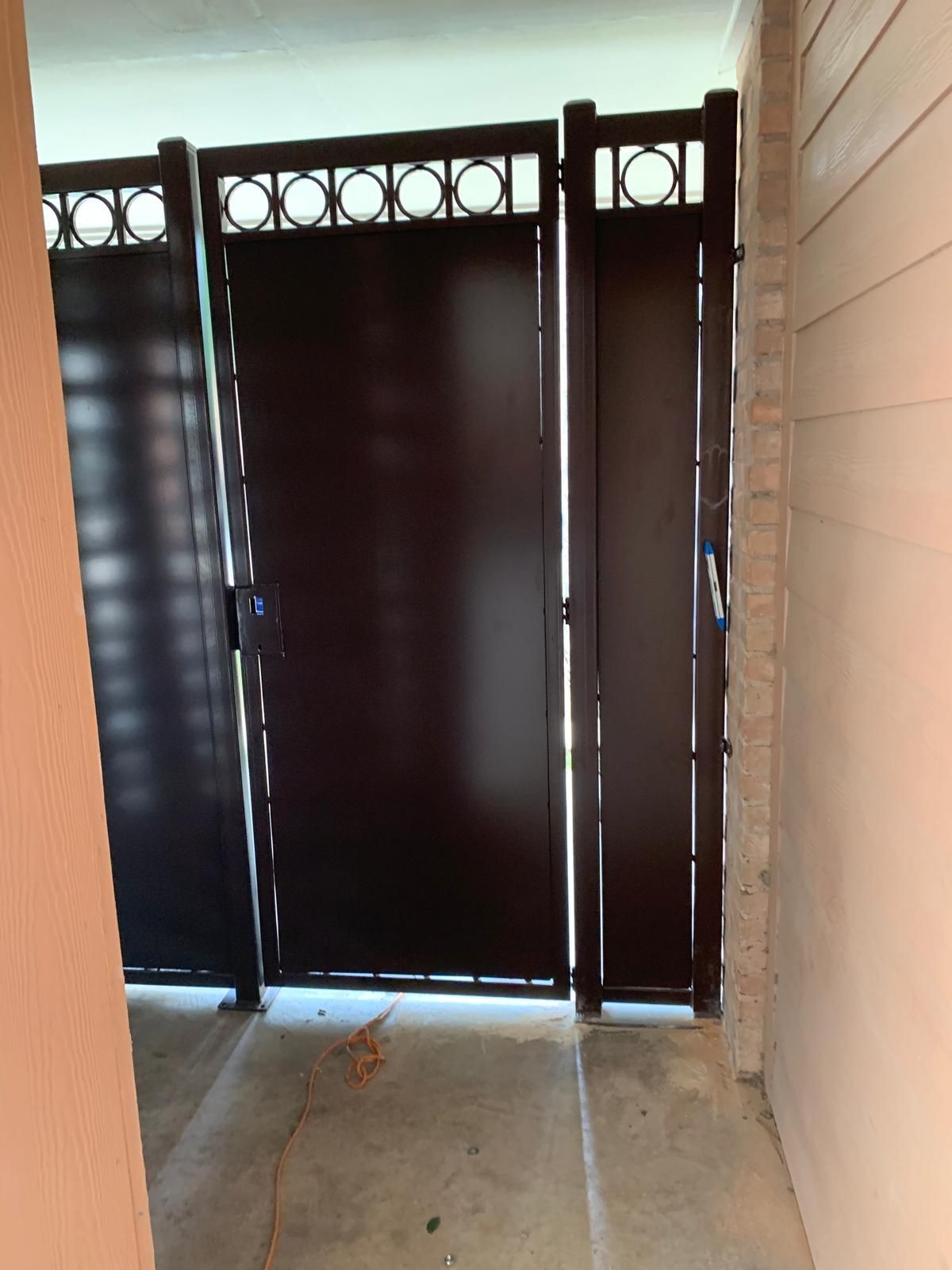 Black metal gate with decorative circles, set in a concrete opening between beige walls.