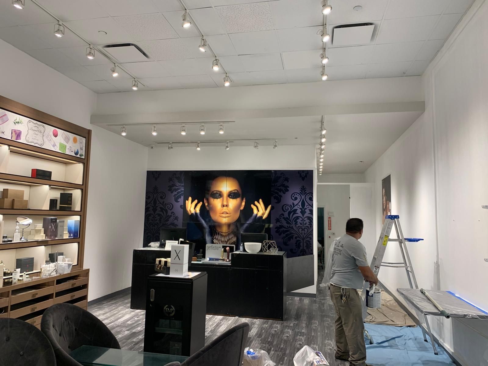 A person on a ladder in a retail store, with a large wall advertisement and products displayed on shelves.