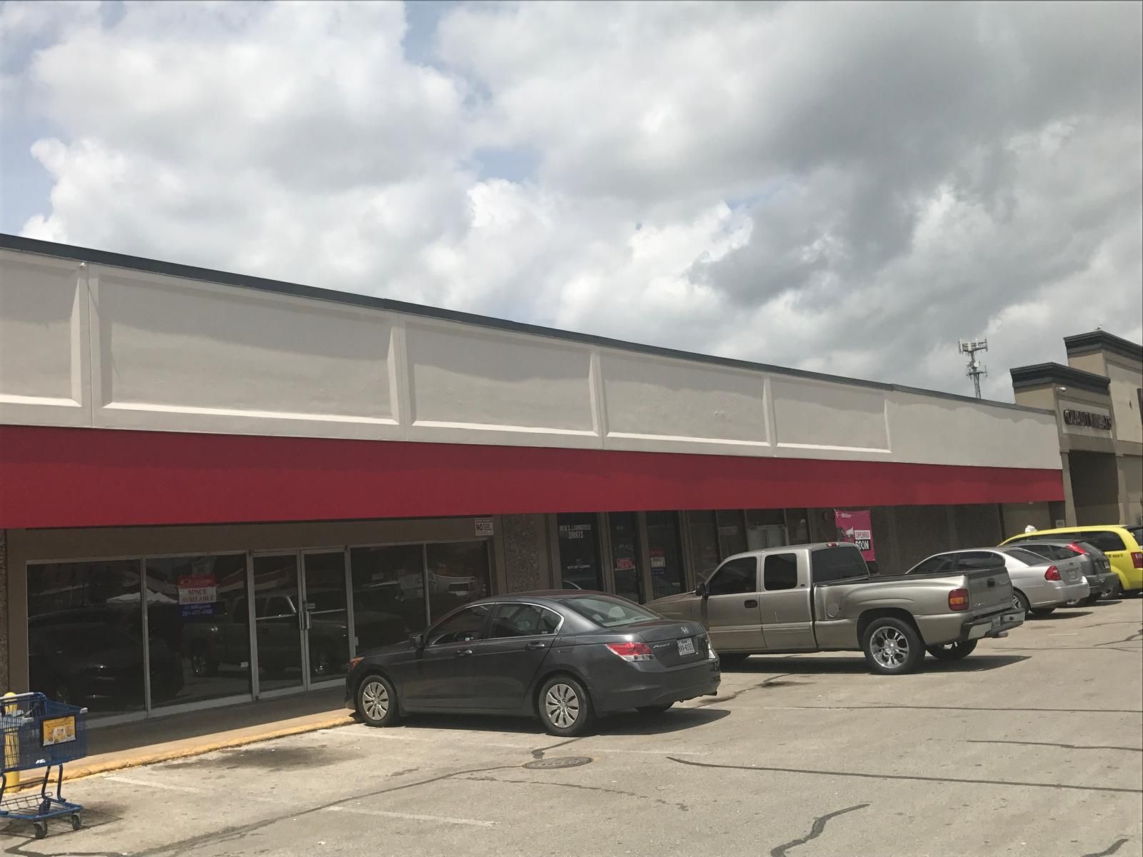 A long, low, red-trimmed building with cars parked in front; cloudy sky overhead.