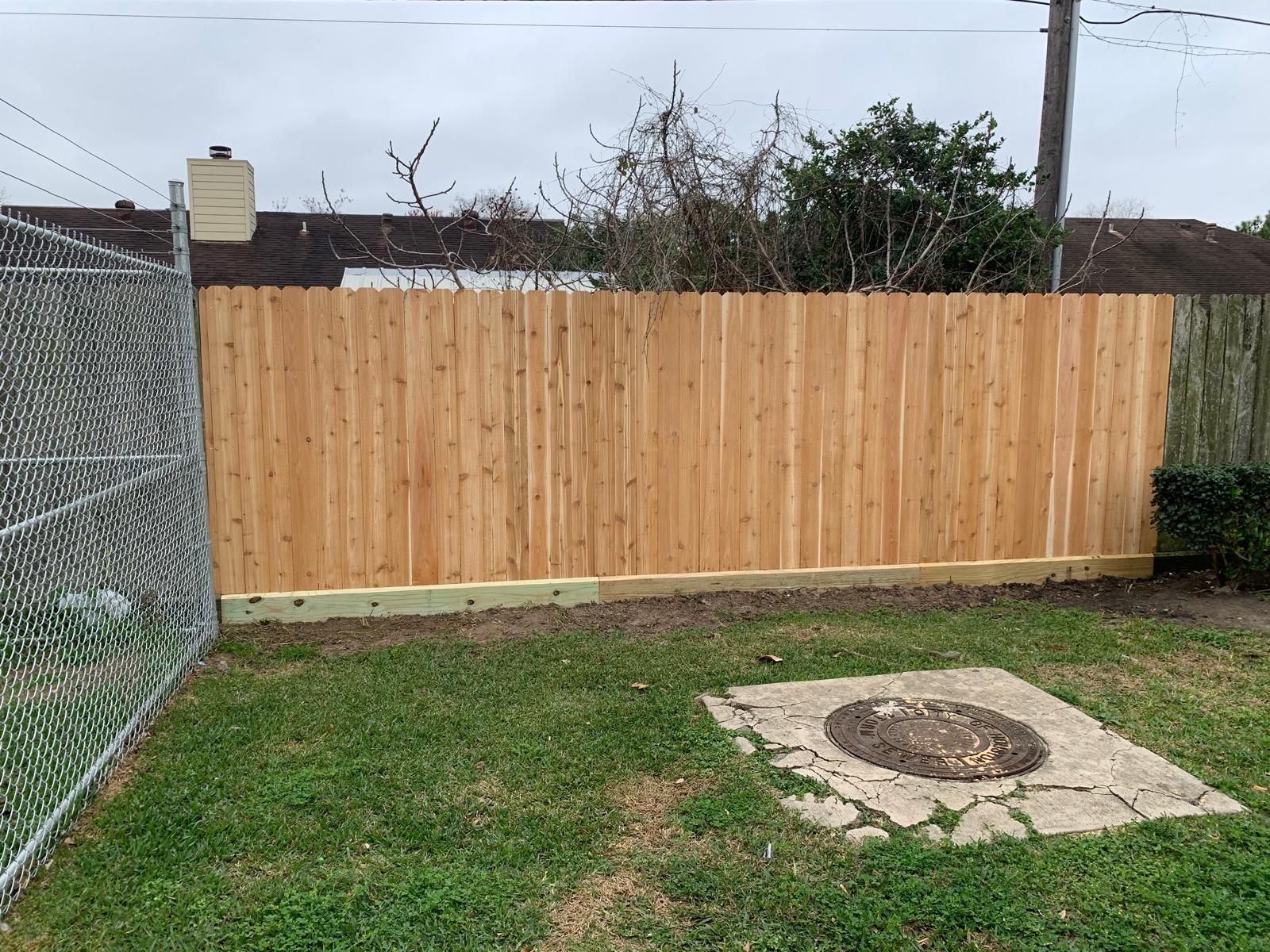 Wooden fence in a yard with a grassy lawn and a concrete utility access.