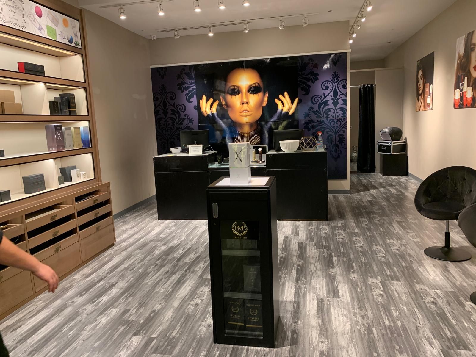 Interior of a shop, featuring display cases and a promotional backdrop of a woman's face. Gray flooring and lighting.