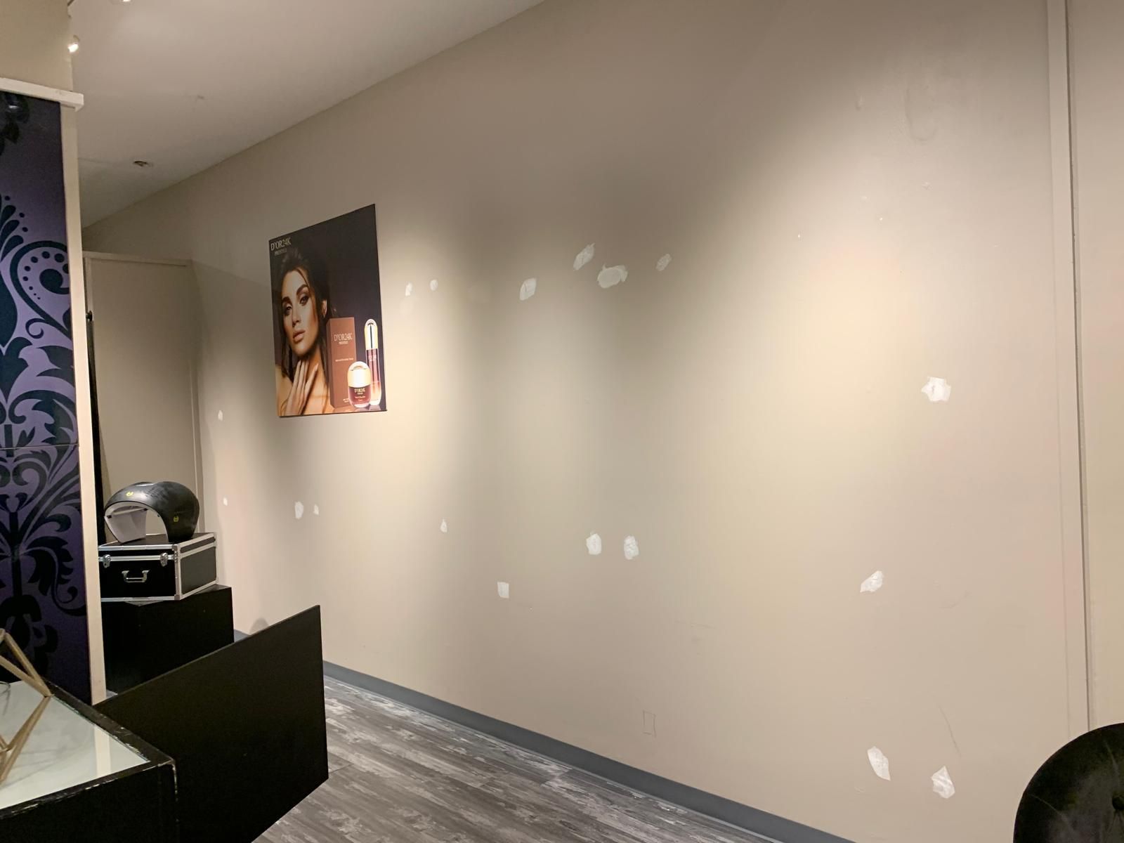 Beige wall with numerous white patches; a photo and display stand are visible in a room.