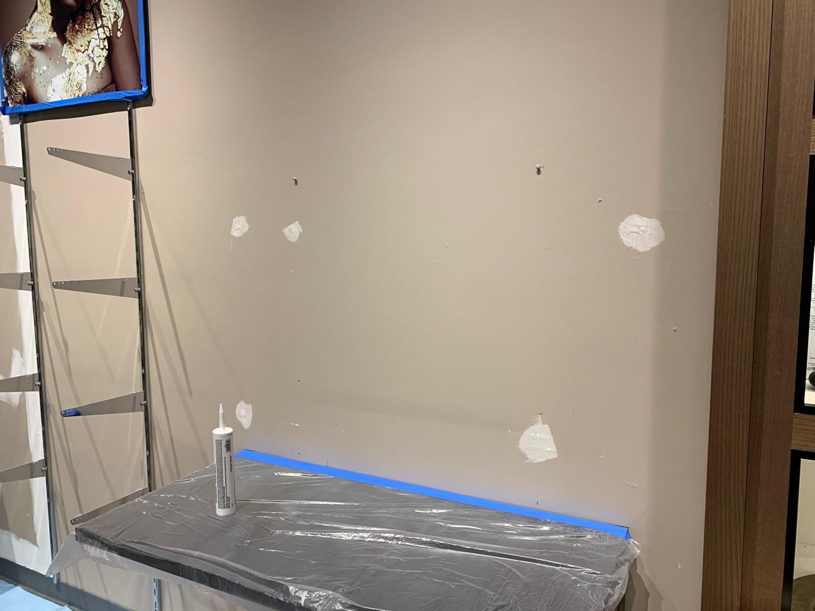 Beige wall with spackled holes, a covered surface, and a caulk tube.